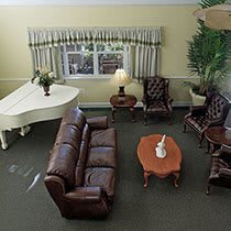 A cozy living room with a white piano, leather couch, chairs, and a wooden coffee table.