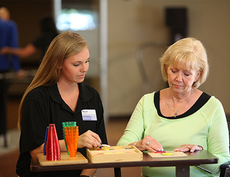 A young adult assists an elderly person with a tabletop activity, fostering engagement and interaction.
