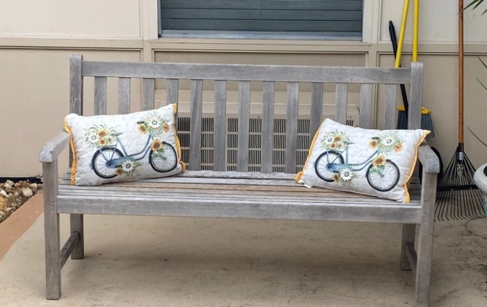 A wooden outdoor bench adorned with two decorative pillows featuring bicycle designs.