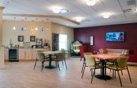 A cozy cafe interior with tables and chairs arranged on a wooden floor, featuring warm lighting and decor.