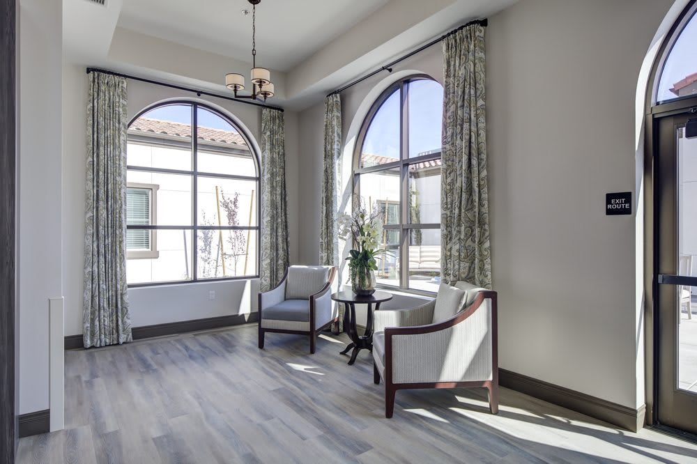 A bright and elegant living space featuring large arched windows, stylish chairs, and chic curtains.