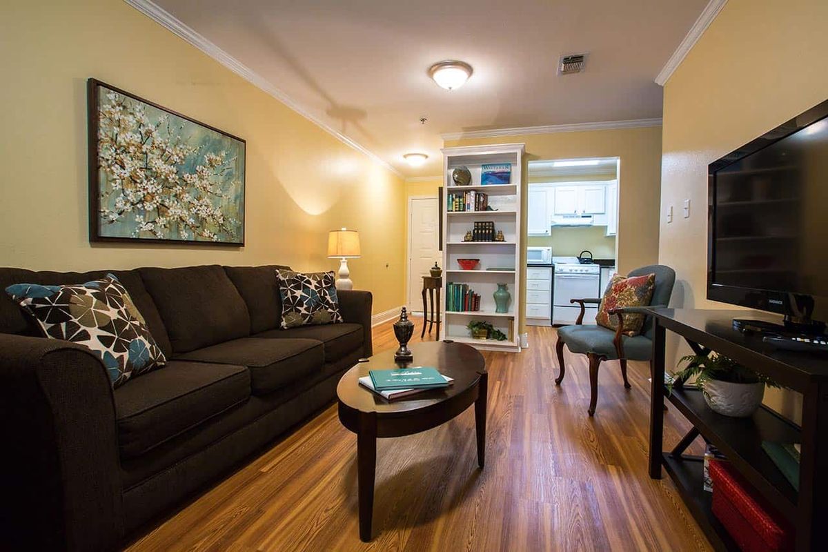 A cozy living room with a dark sofa and a wooden coffee table, leading to a kitchen through a bookshelf partition.