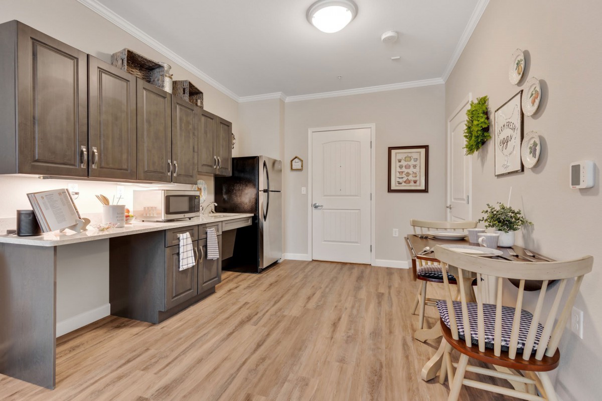 A modern kitchen interior with wooden flooring, dark cabinets, and a small dining area.