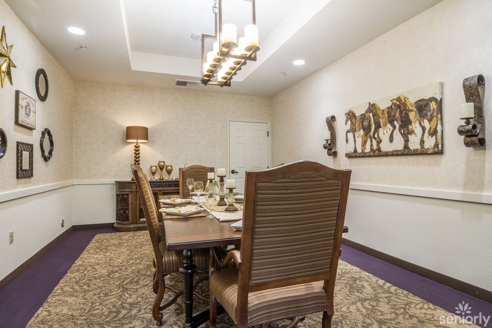 A beautifully decorated dining room with a large table and elegant chairs, featuring artwork on the walls and warm lighting.