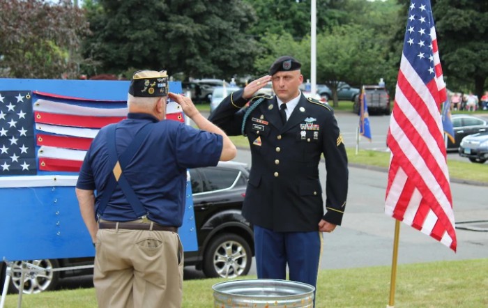 A serviceman in uniform salutes a veteran during an outdoor ceremony.