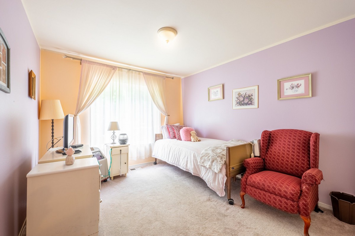 A cozy bedroom with a single bed and purple walls, complemented by an armchair and soft natural lighting.