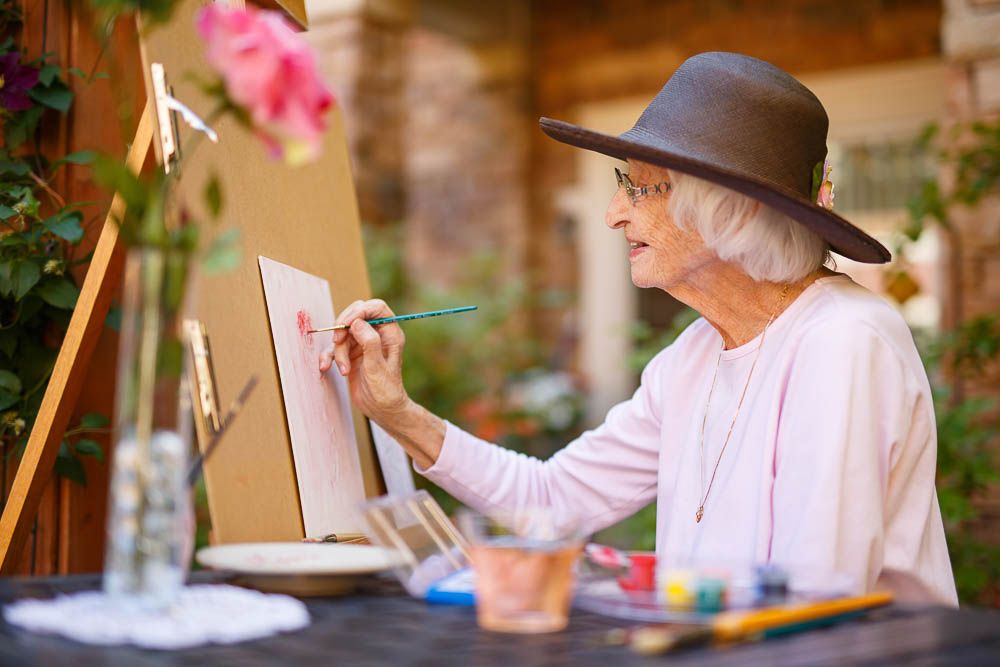 An elderly woman painting outdoors, showcasing her artistic creativity.