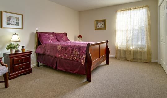 A cozy bedroom featuring a wooden bed with purple bedding and a window allowing natural light.