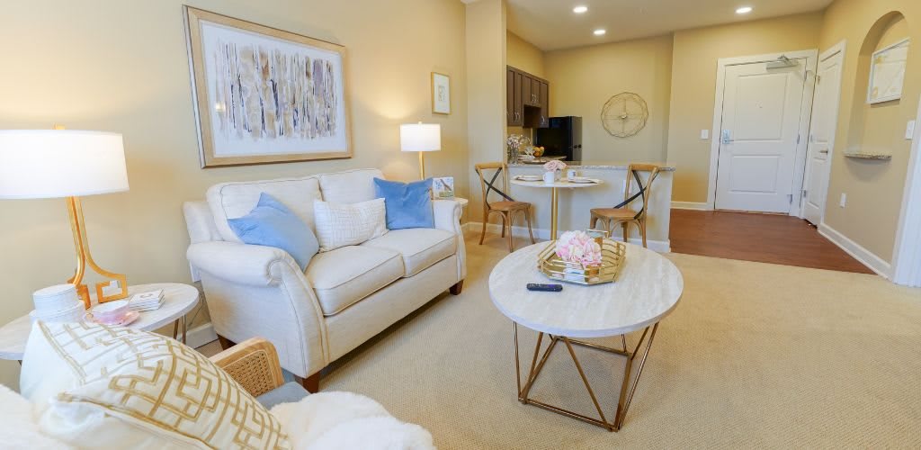 A cozy living room with modern decor, featuring a white sofa, a round marble coffee table, and an open floor plan leading to the kitchen area.