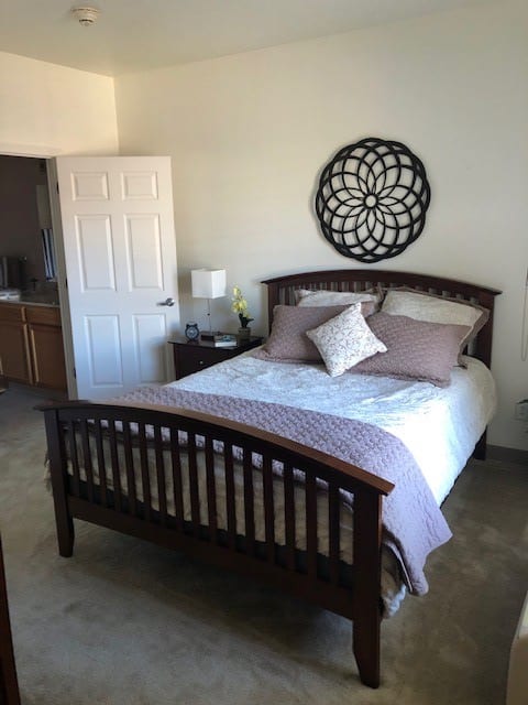 A cozy bedroom with a neatly made bed, decorative wall art, and a nightstand with a lamp.