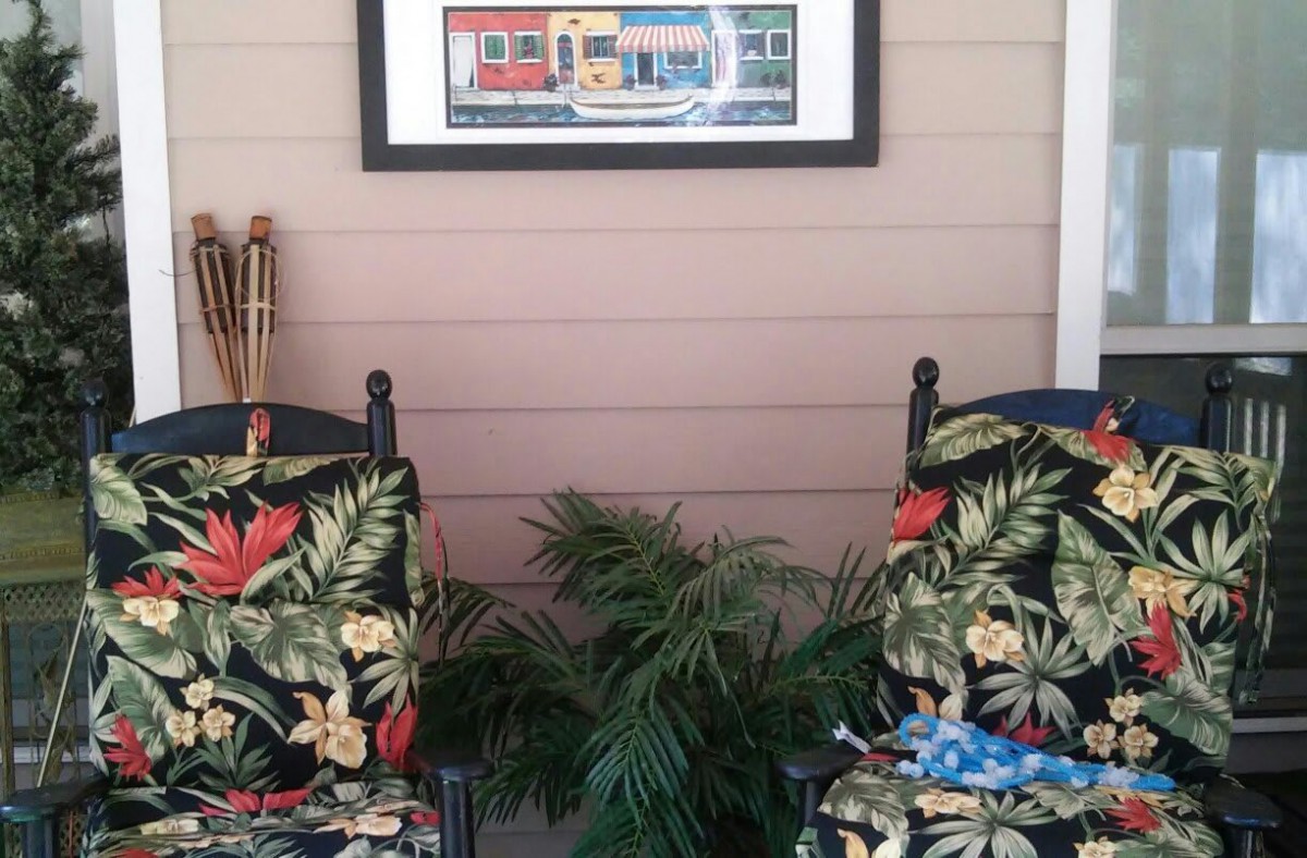 A cozy porch setup with two tropical-themed chairs and a vibrant painting on the wall.