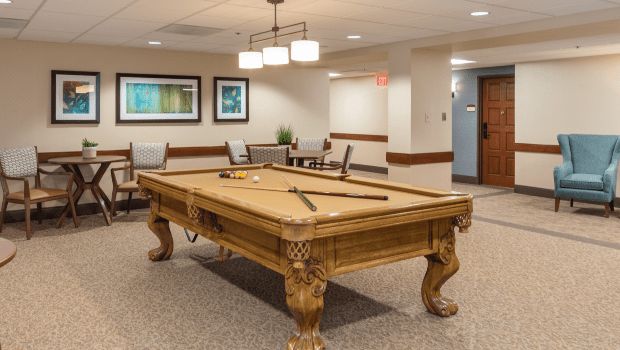 A well-furnished game room featuring a classic wooden pool table with cues and balls arranged on top.