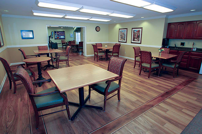 An empty dining room with wooden tables and chairs, featuring wood flooring and soft lighting.