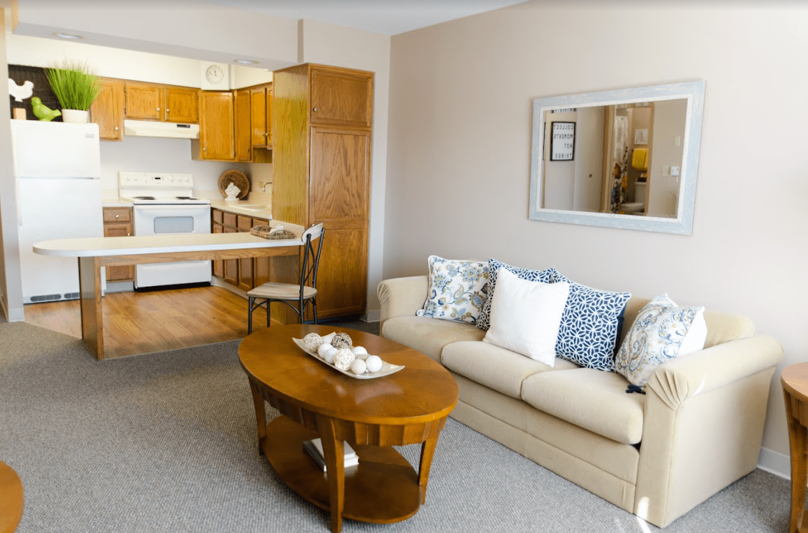 A cozy living room with an open view to the kitchen, featuring a beige sofa and a wooden coffee table.