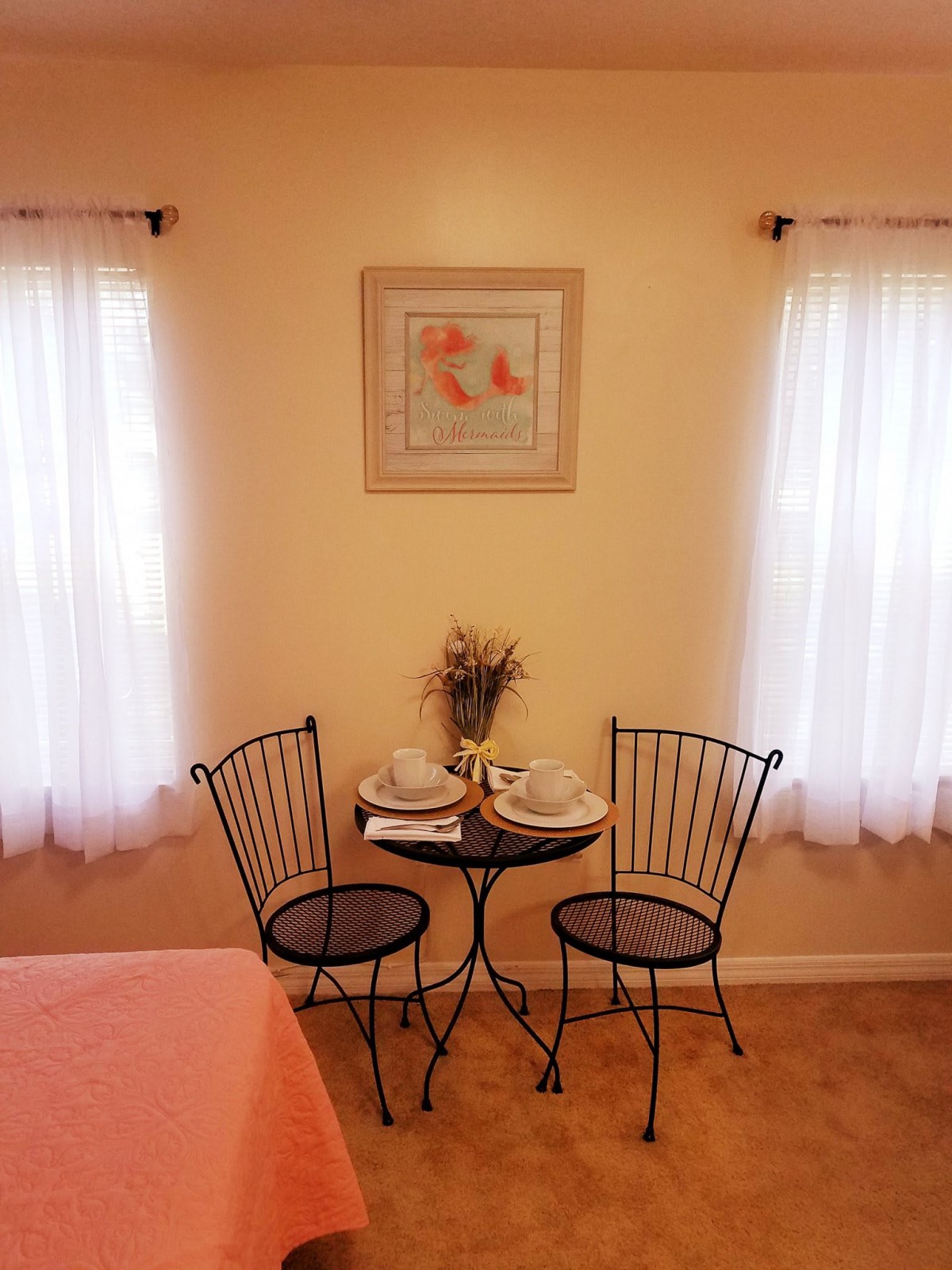 A cozy corner with a small table and two chairs, framed by soft window curtains and wall art.