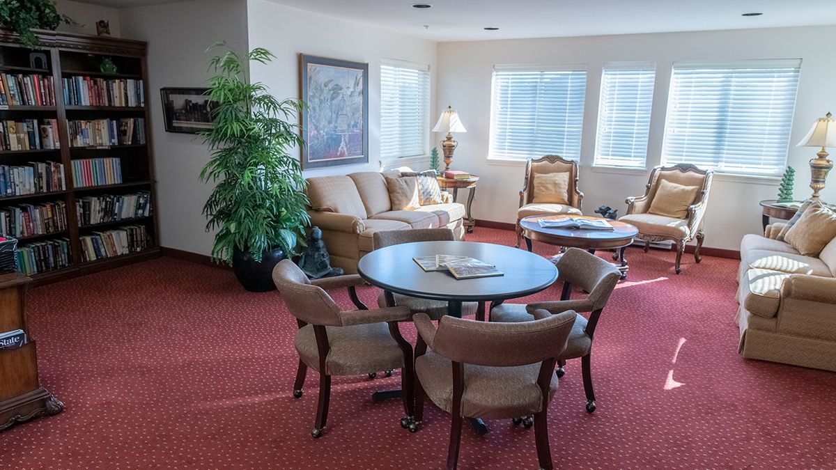 A cozy living room with comfortable seating, a round table, and natural light from the windows.