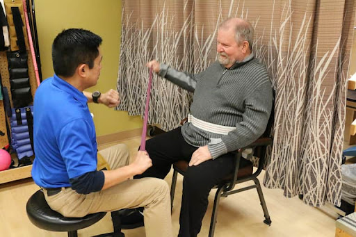 A therapist assists an elderly patient with a stretching exercise using resistance bands during a physical therapy session.