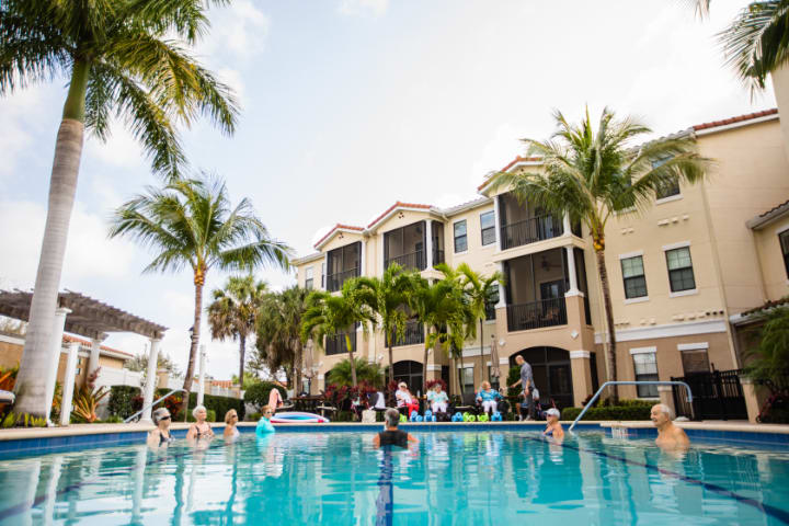 Residents enjoy a sunny day at the apartment complex pool surrounded by palm trees.