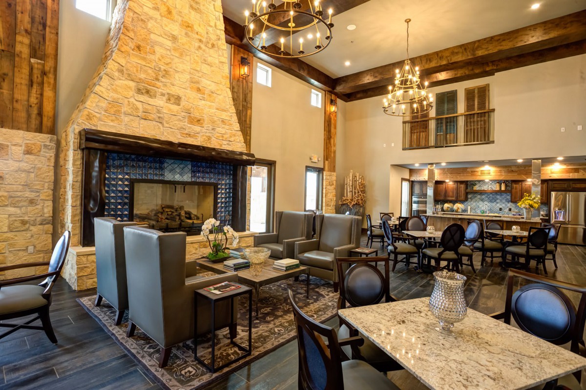 A spacious living room featuring a large stone fireplace, elegant chandeliers, and comfortable seating.