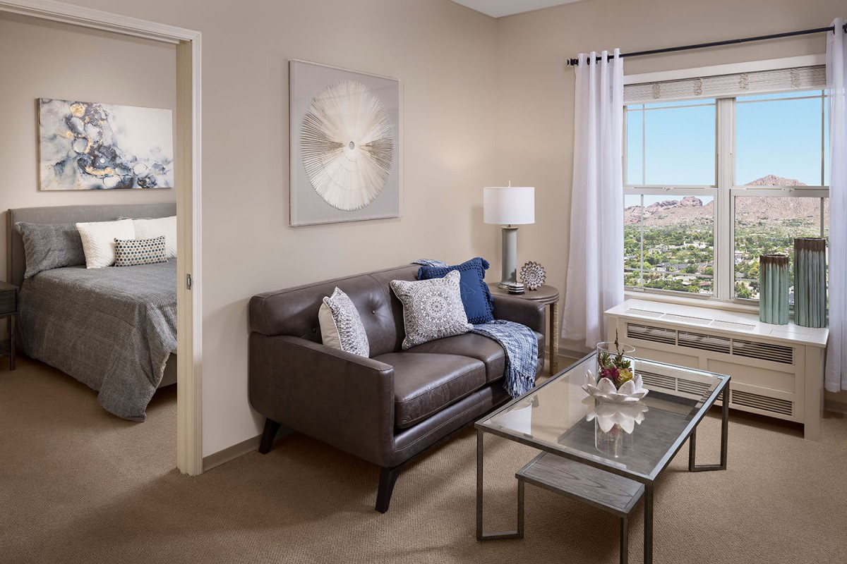 A cozy living room with a dark sofa, a glass coffee table, and natural light from the window.