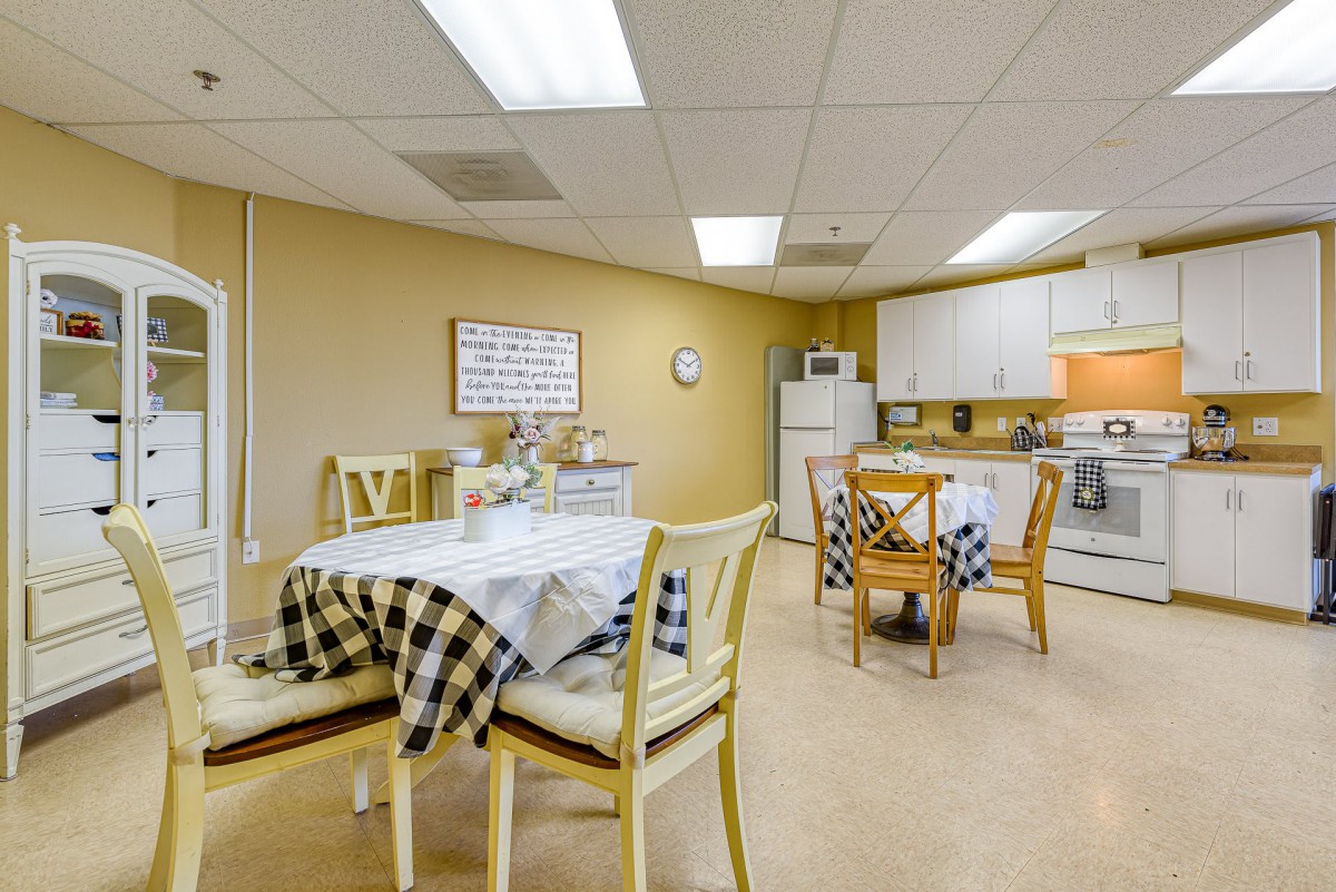 A cozy kitchen and dining area featuring checkered tablecloths, multiple tables and chairs, and various kitchen appliances.