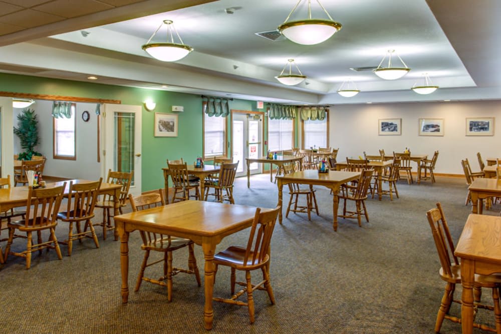 A spacious dining room with wooden tables and chairs, featuring soft lighting and a carpeted floor.