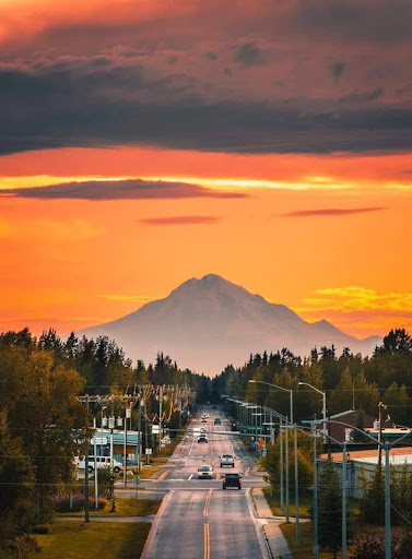 A serene view of a mountain at sunset, framed by a quiet road and lined with trees.