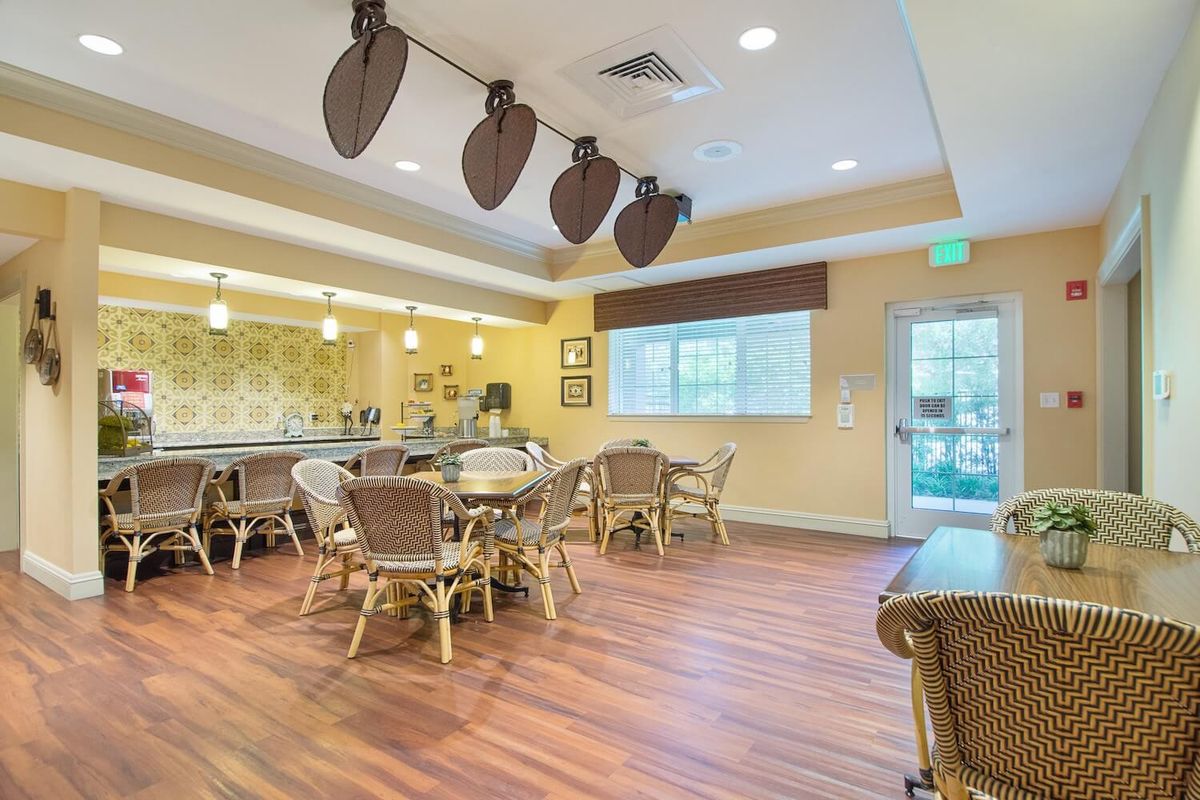 A cozy dining area with wooden floors, tables, and chairs, adorned with ceiling fans and ample lighting.
