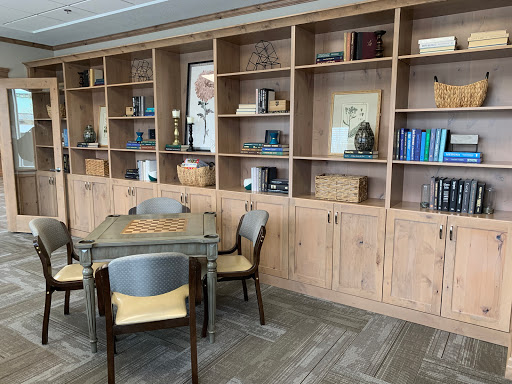 A cozy workspace featuring a wooden table surrounded by chairs and a neatly organized bookshelf.