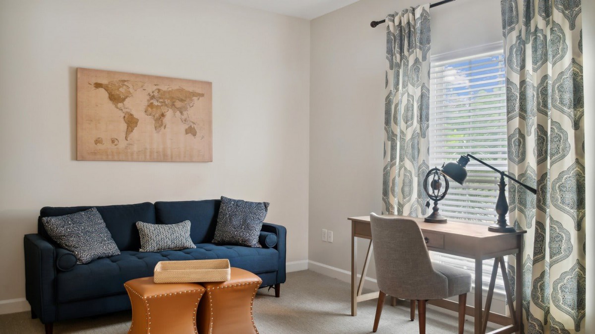 A cozy living room with a blue sofa, wooden coffee table, and a workspace featuring a desk and chair by the window.