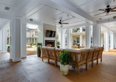 A stylish outdoor living space featuring a bar area with wooden chairs, a fireplace, and a television under a ceiling fan.