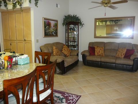 A cozy living room with two sofas, a dining table with chairs, and decorative elements including a ceiling fan and wall art.
