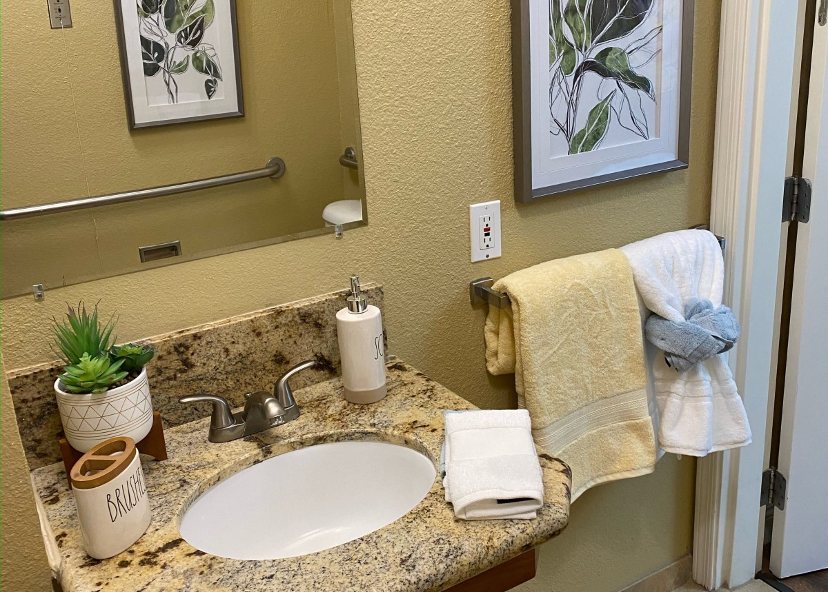 A neatly organized bathroom with a granite countertop, featuring a sink, towels, and decorative artwork on the wall.