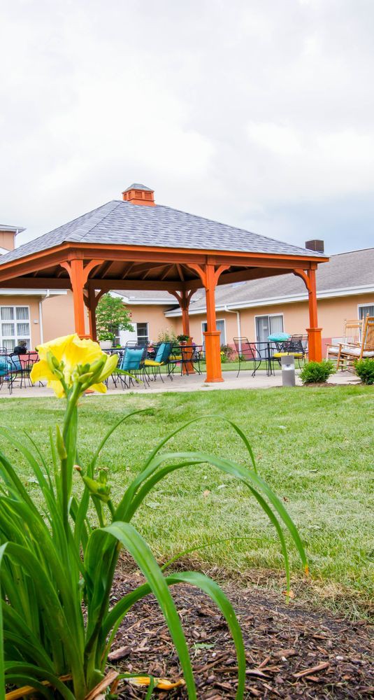 A sunny garden with a gazebo and outdoor seating surrounded by a lush lawn and blooming flowers.