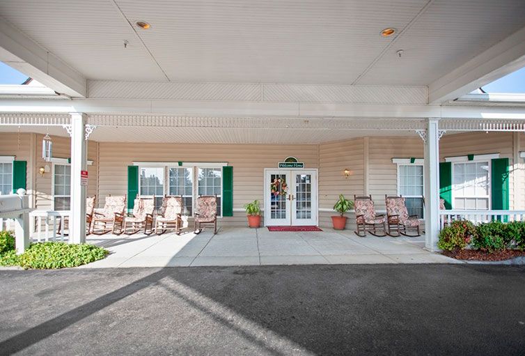 The exterior entrance of a building featuring chairs and potted plants under a covered walkway.