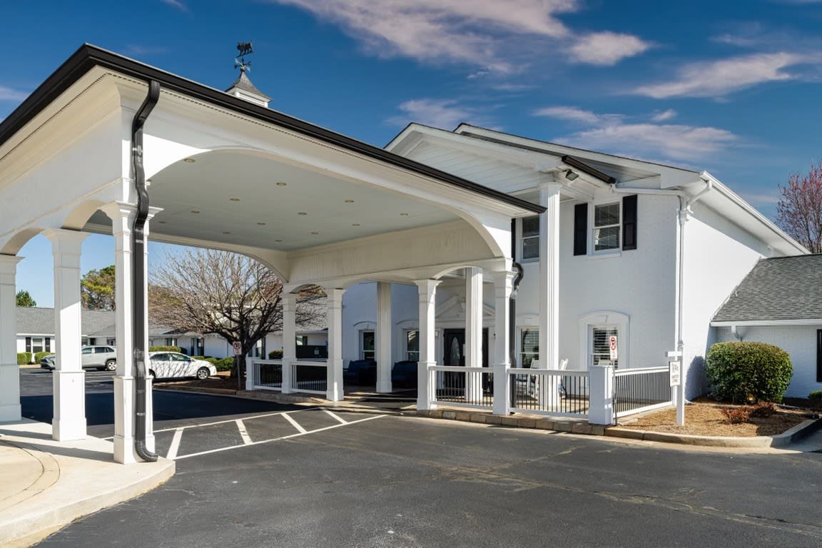 A two-story building with a covered entrance supported by columns and a surrounding parking area.