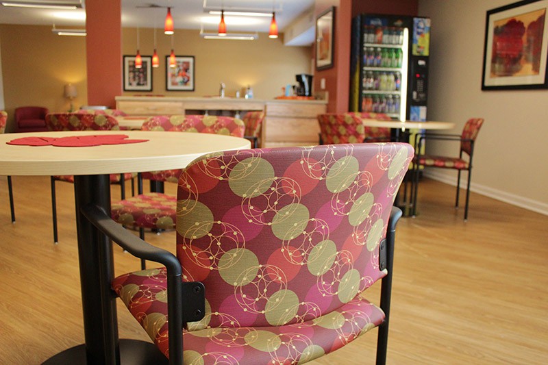 A cozy cafe interior with patterned chairs and tables, featuring a vending machine in the background.