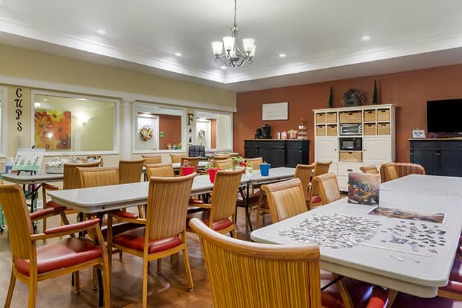 A community room with tables and chairs arranged for activities, featuring a puzzle in progress.