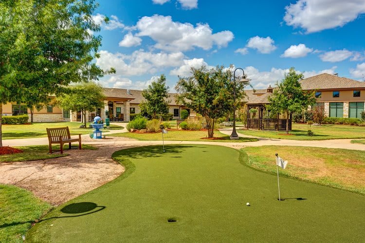A well-maintained outdoor mini golf course on a sunny day, featuring a putting green and surrounding benches.