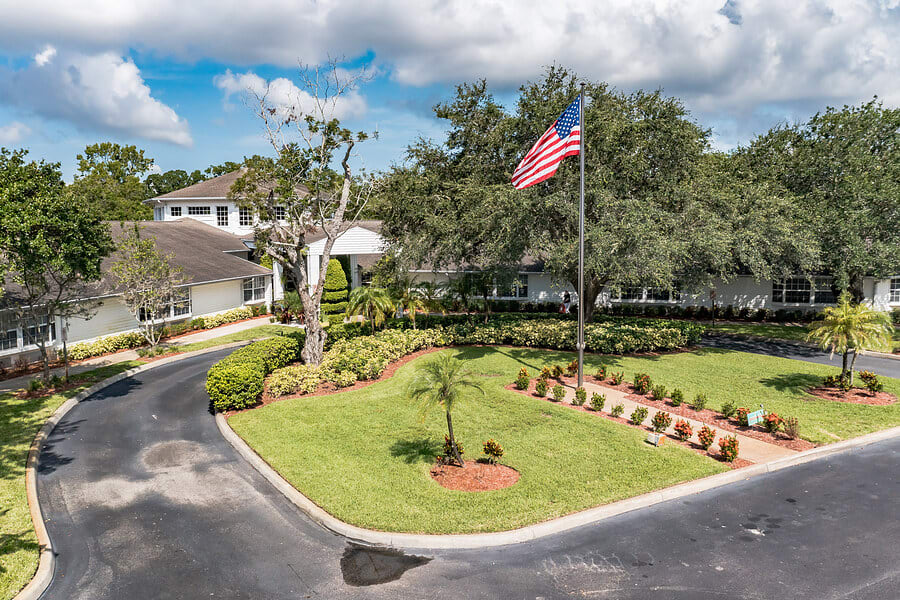A building with a landscaped entrance, featuring an American flag and surrounded by trees and greenery.