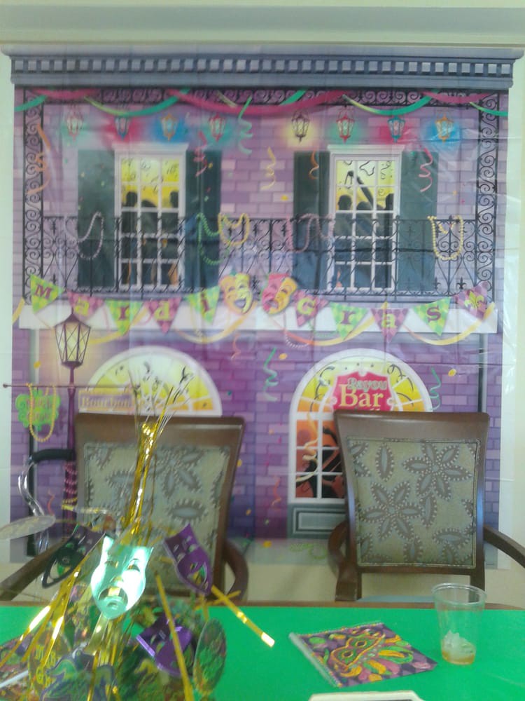 A festive Mardi Gras-themed room with colorful decorations and two chairs in front of a party backdrop.