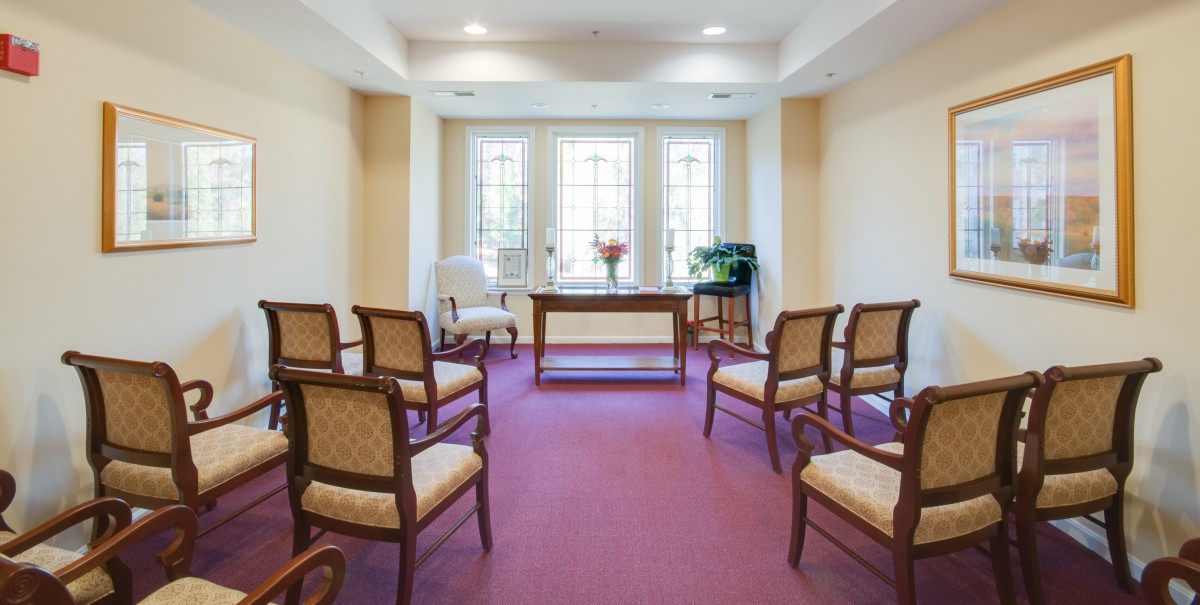 A bright waiting room featuring a row of chairs, a central table, and large windows allowing natural light.