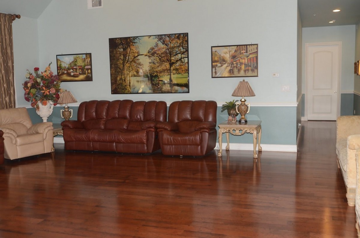 A cozy living room featuring a brown leather sofa, decorative paintings on the wall, and elegant lamps on side tables.