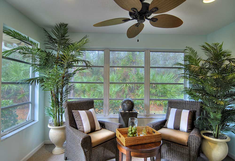 A cozy sunroom featuring wicker chairs, tropical plants, and large windows with abundant natural light.