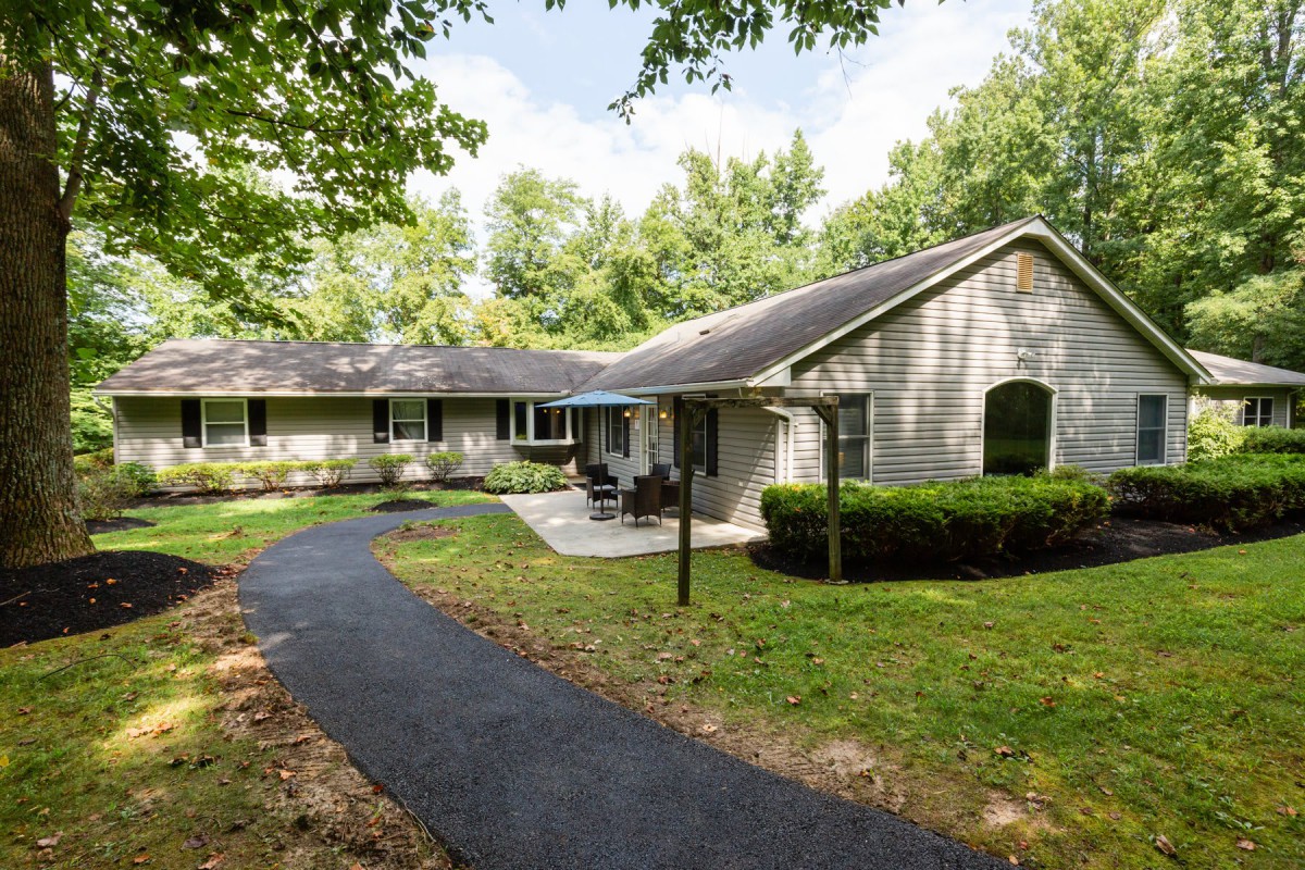 A single-story house with a well-maintained lawn and a curved driveway surrounded by trees.