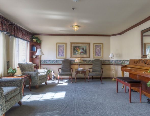 A cozy living room featuring comfortable chairs, a piano, and decorative artwork on the walls.