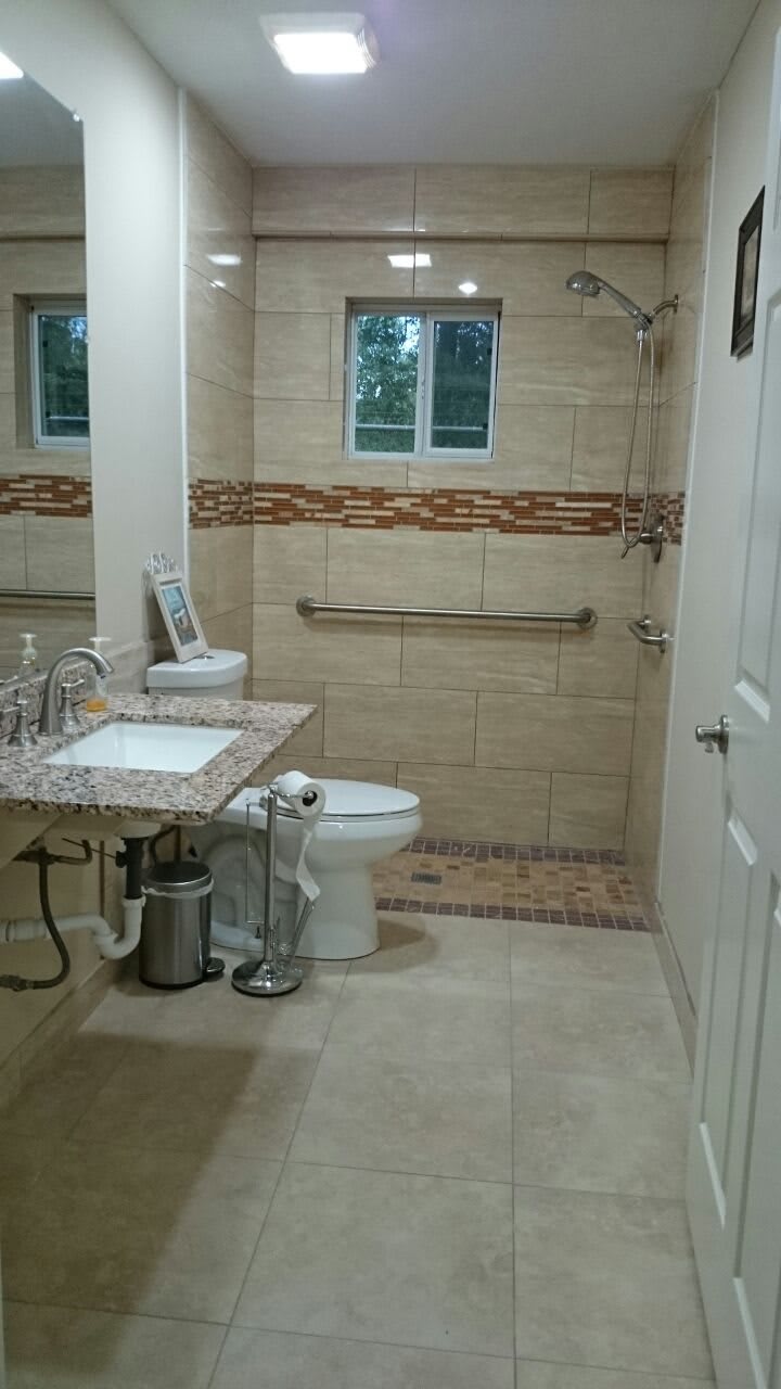 A modern bathroom featuring a sink, toilet, and mirror with tiled walls.