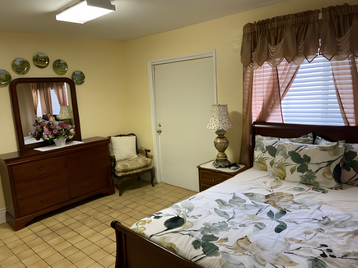A cozy bedroom with floral bedding, a wooden dresser, and a mirror.