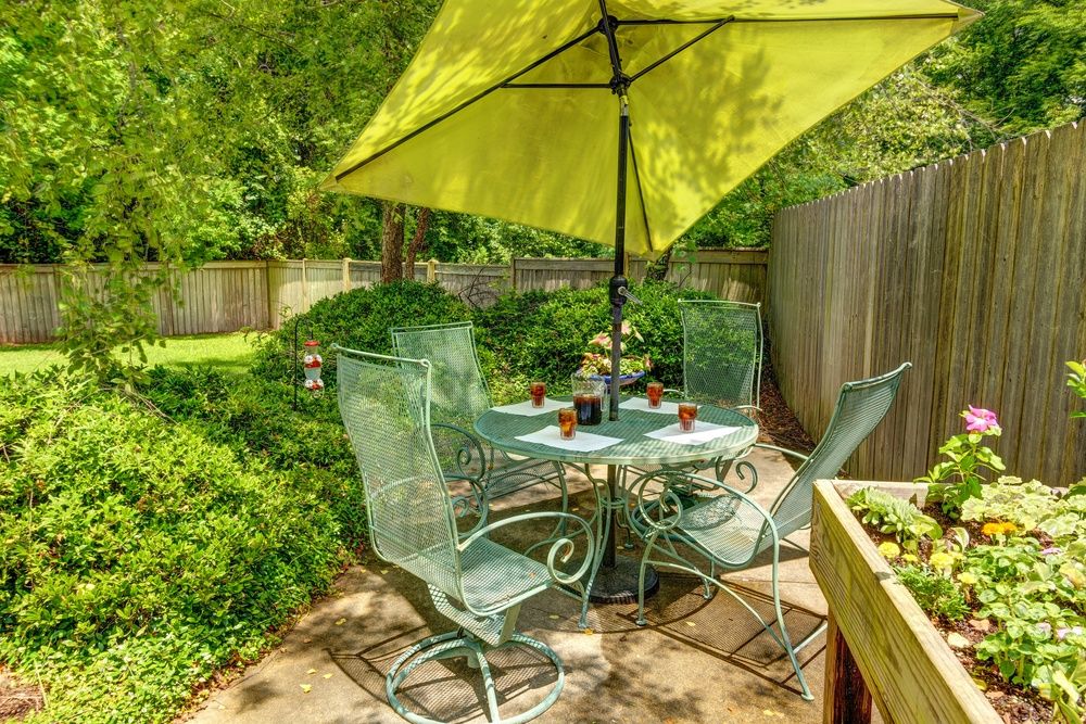 A cozy garden patio with a table and chairs set under a large green umbrella.