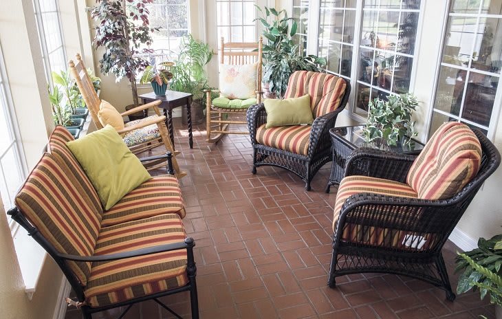 A cozy sunroom with wicker furniture and striped cushions surrounded by plants.